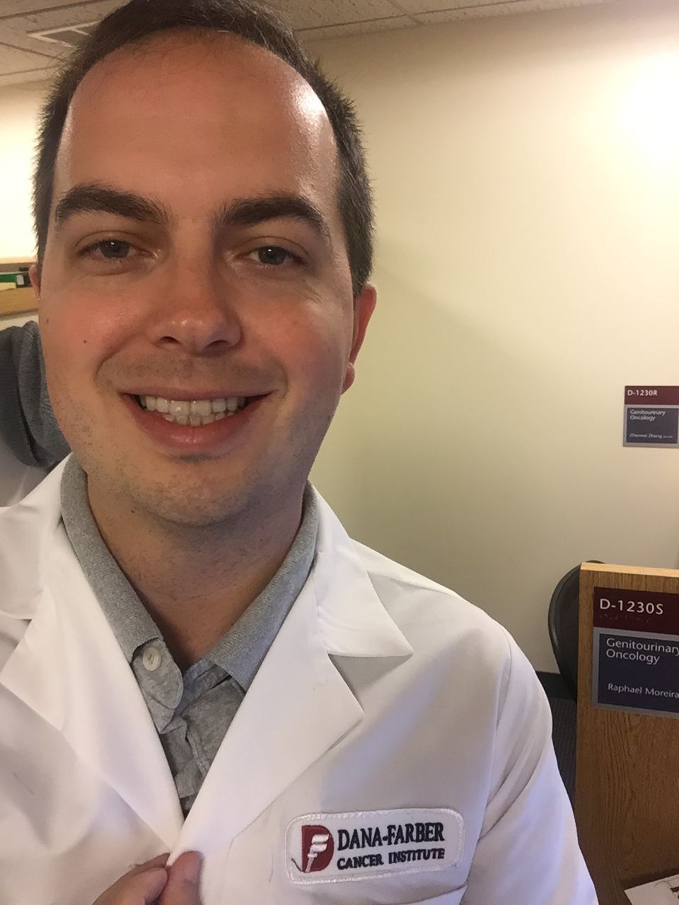 Dr. Raphael de jaleco Dana-Farber na frente da placa da sala