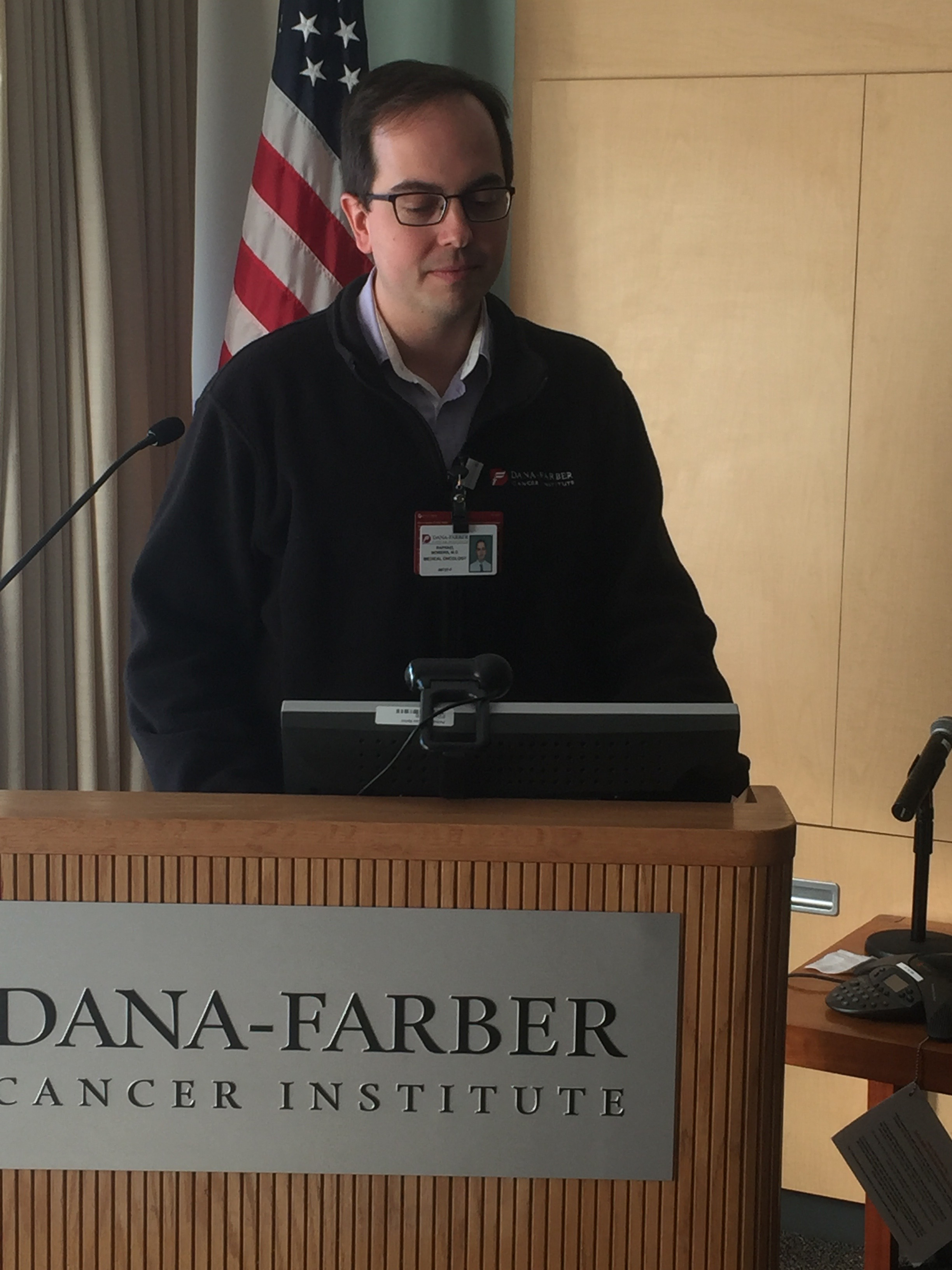 Dr. Raphael apresentando no Dana-Farber com bandeira americana ao fundo